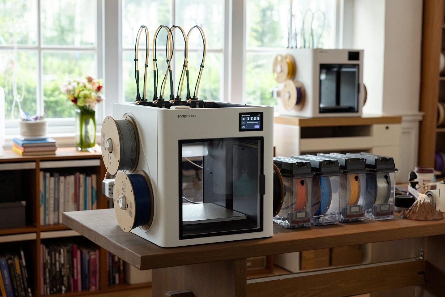 Una stampante 3D bianca con bobine di filamento su un tavolo di legno.